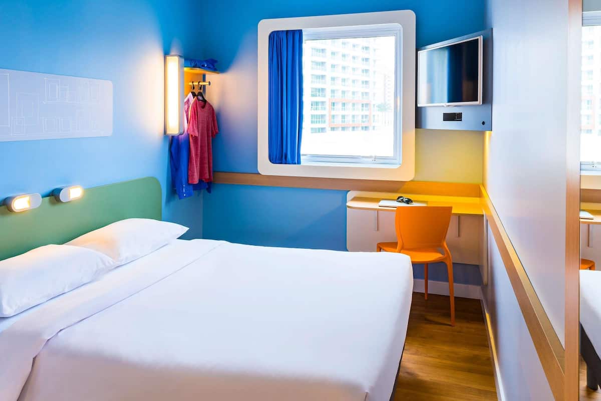 Een hotelkamer met een bed, een bureau, een stoel, een televisie en een raam met gordijnen.