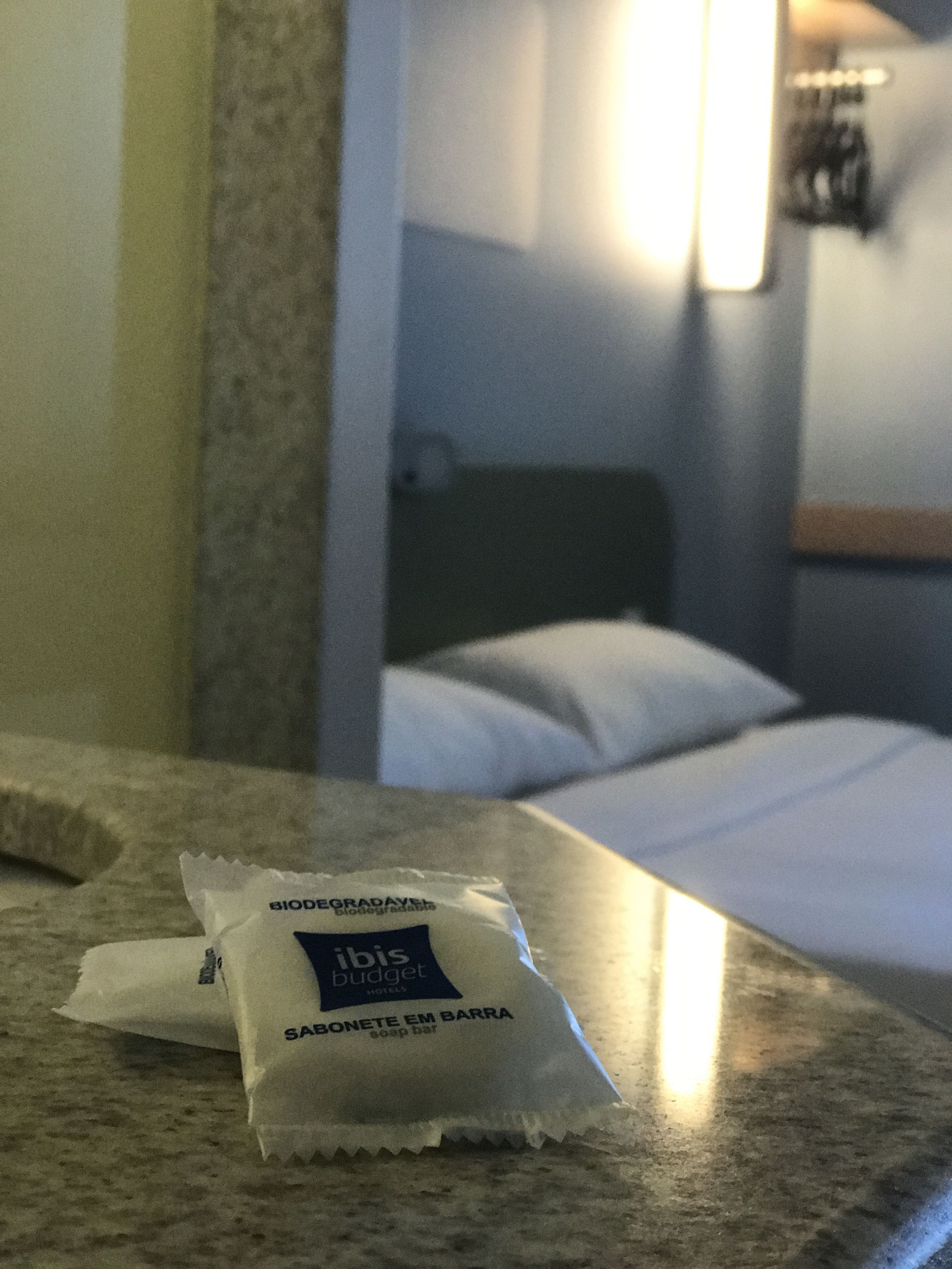 A hotel room with a bed, a nightstand, and a packet of soap bar on the counter.