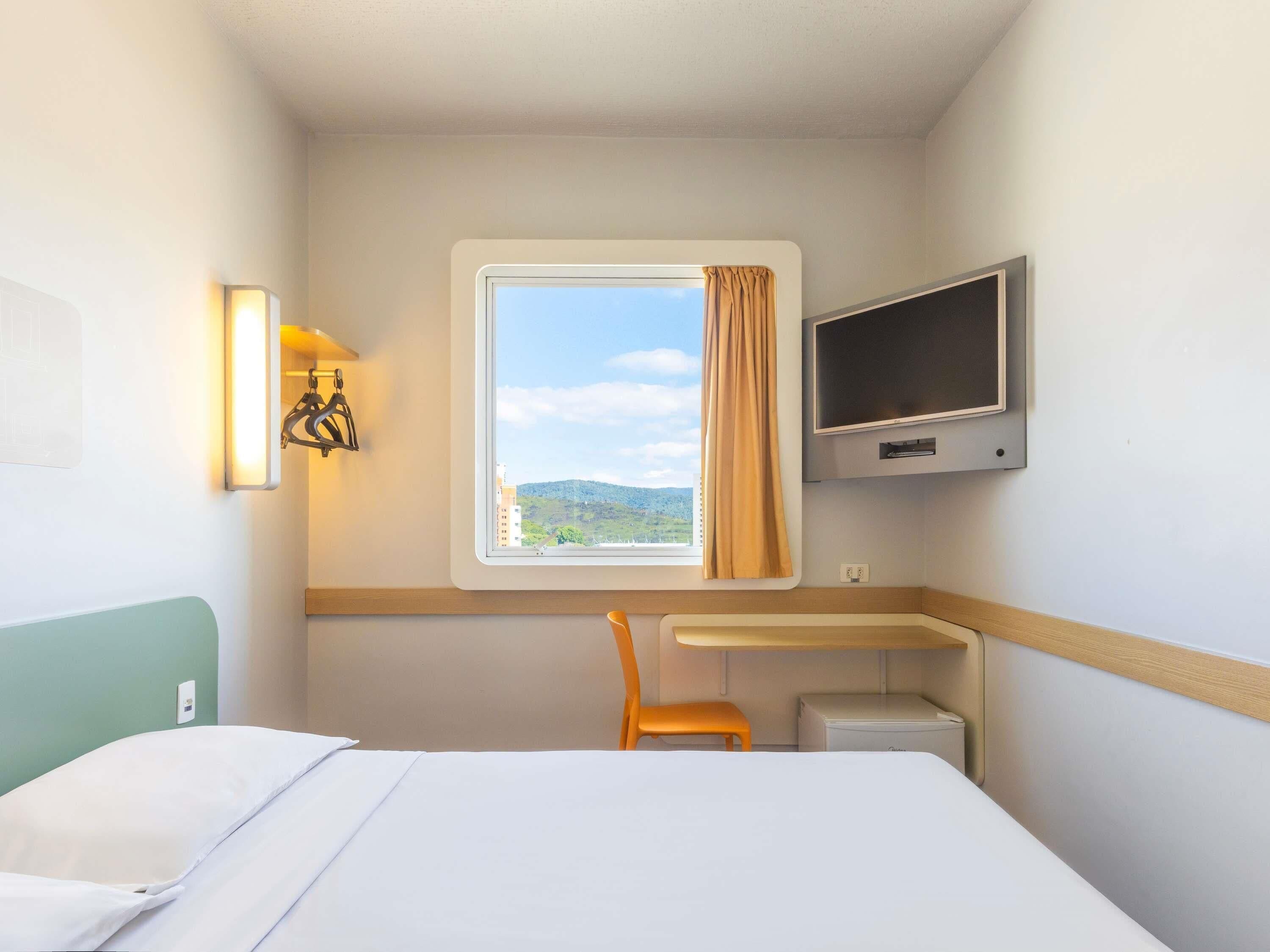 A hotel room with a bed, a desk, a chair, a TV, and a window with a view of the outdoors.