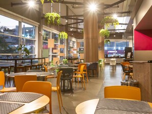 Ein modernes Café-Interieur mit Tischen, Stühlen, hängenden Pflanzen und großen Fenstern.