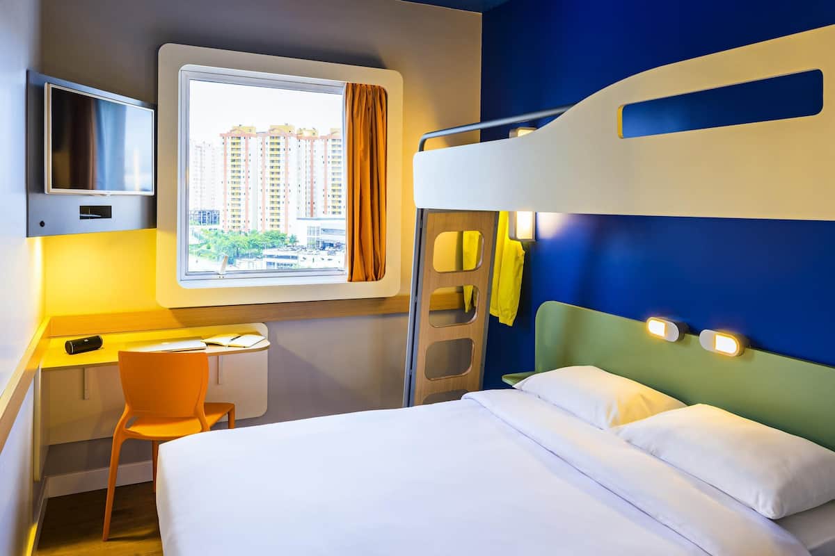 Habitación de hotel con literas, un escritorio con silla, televisión y ventana con cortinas.