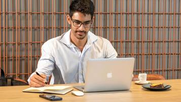 Uma pessoa sentada à mesa de madeira com um laptop, um caderno e um smartphone.