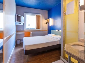 Une chambre d’hôtel comprenant un lit, un bureau, une chaise, une fenêtre avec des rideaux, une télévision et une salle de bain avec un lavabo.