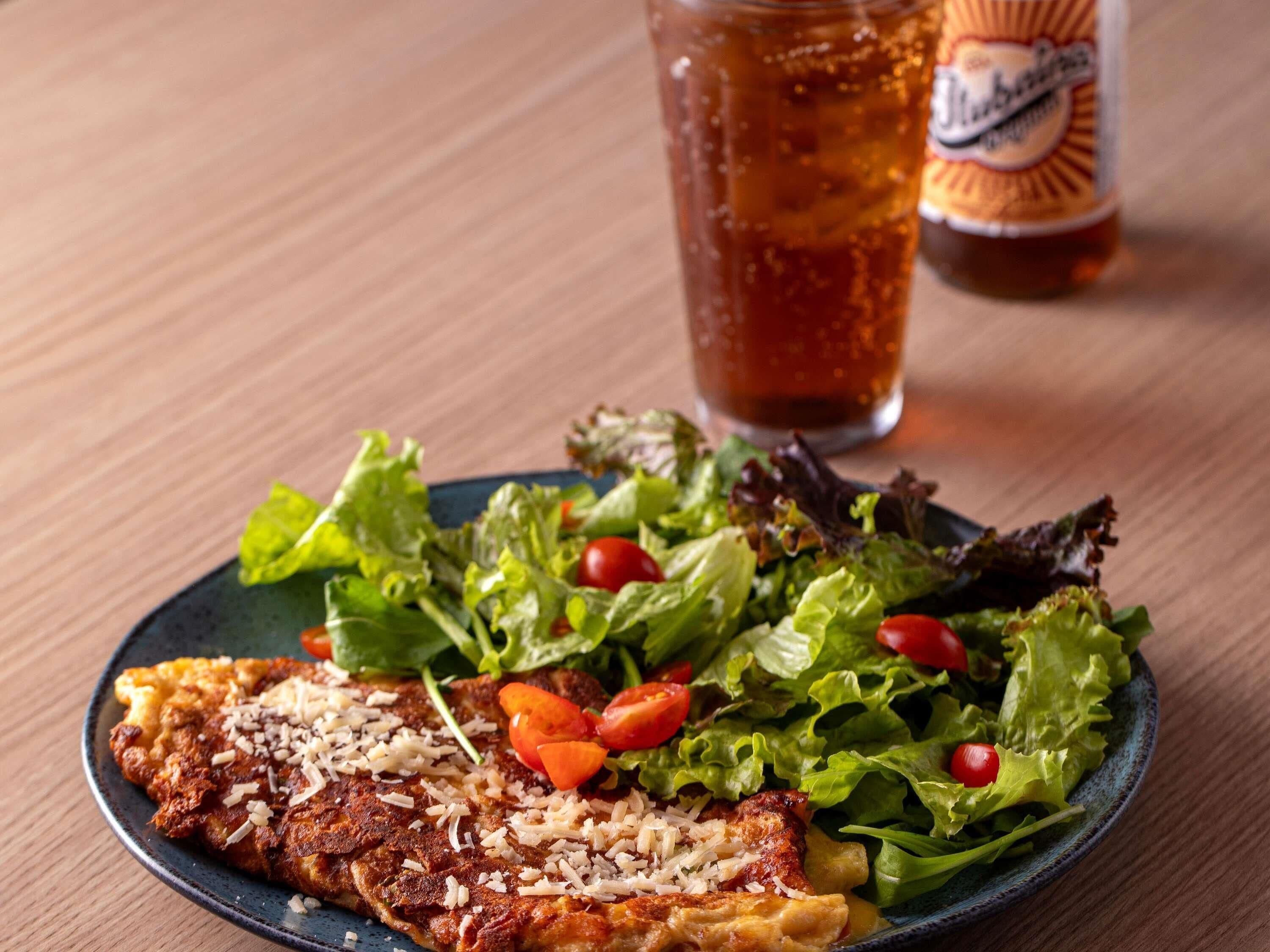 Un plato con pechuga de pollo a la parrilla, una ensalada y un vaso de té helado sobre una mesa de madera.