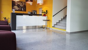 Ein Empfangsbereich mit Theke, einer Uhr, einer Pflanze und einer Treppe.
