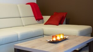 Ein modernes Wohnzimmer mit einem hellen Sofa, einem Holztisch mit Kerzen und roten Zierkissen.