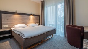 Ein Hotelzimmer mit Bett, Nachttischen, einem Sessel und einem großen Fenster mit Vorhängen.