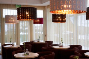 A restaurant with round tables and chairs, large hanging pendant lights, and a view through sheer curtains. - Vila Labas Rytas (Palanga)