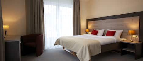 Habitación de hotel con una cama grande, dos mesitas de noche con lámparas, un escritorio con una silla y un ventanal con cortinas.