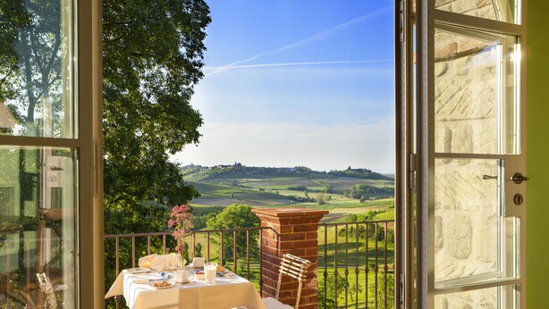 Un balcon avec une table dressée pour le dîner, offrant une vue panoramique sur la campagne environnante.