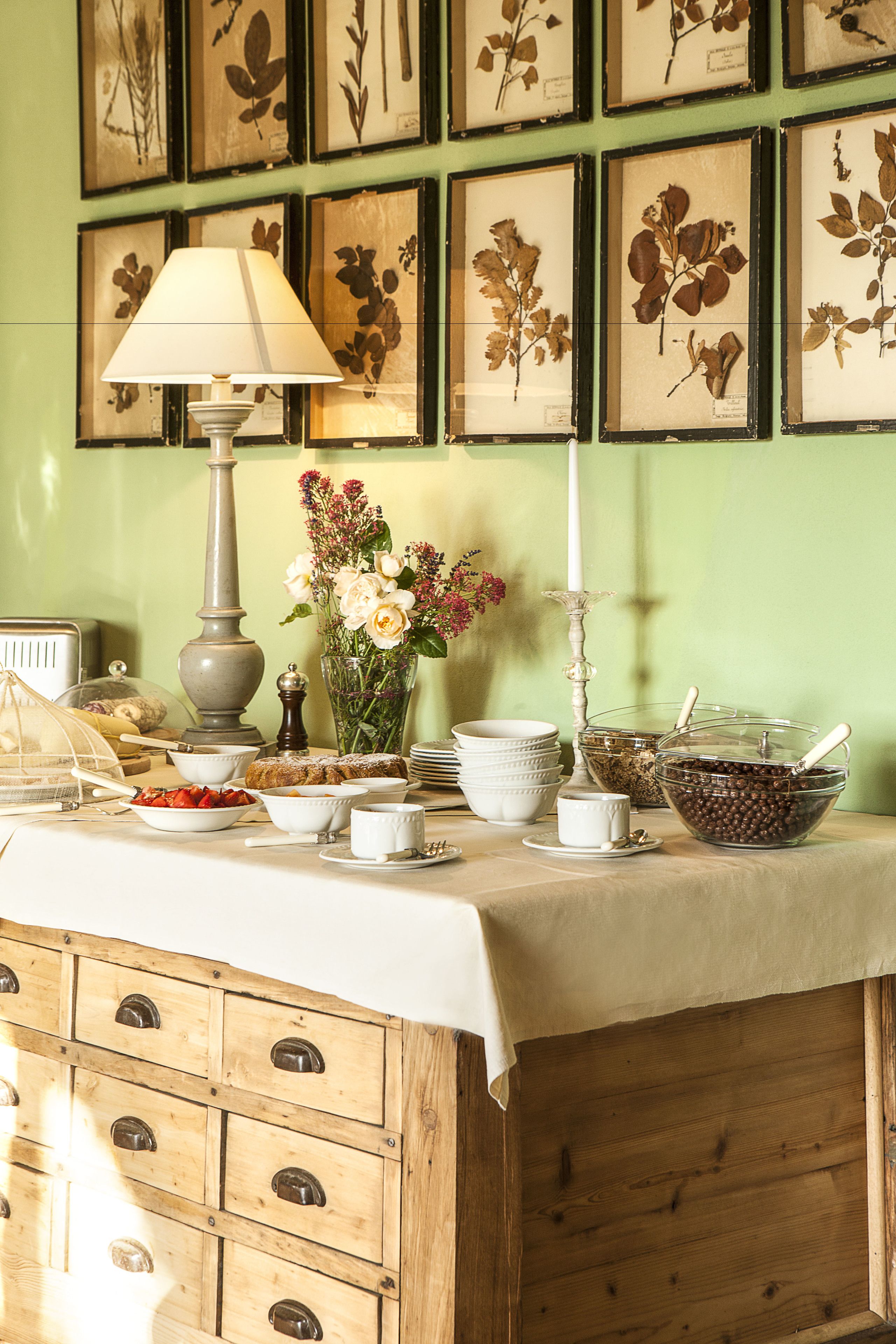 A dining table with a lamp, a vase of flowers, and various dishes and utensils.