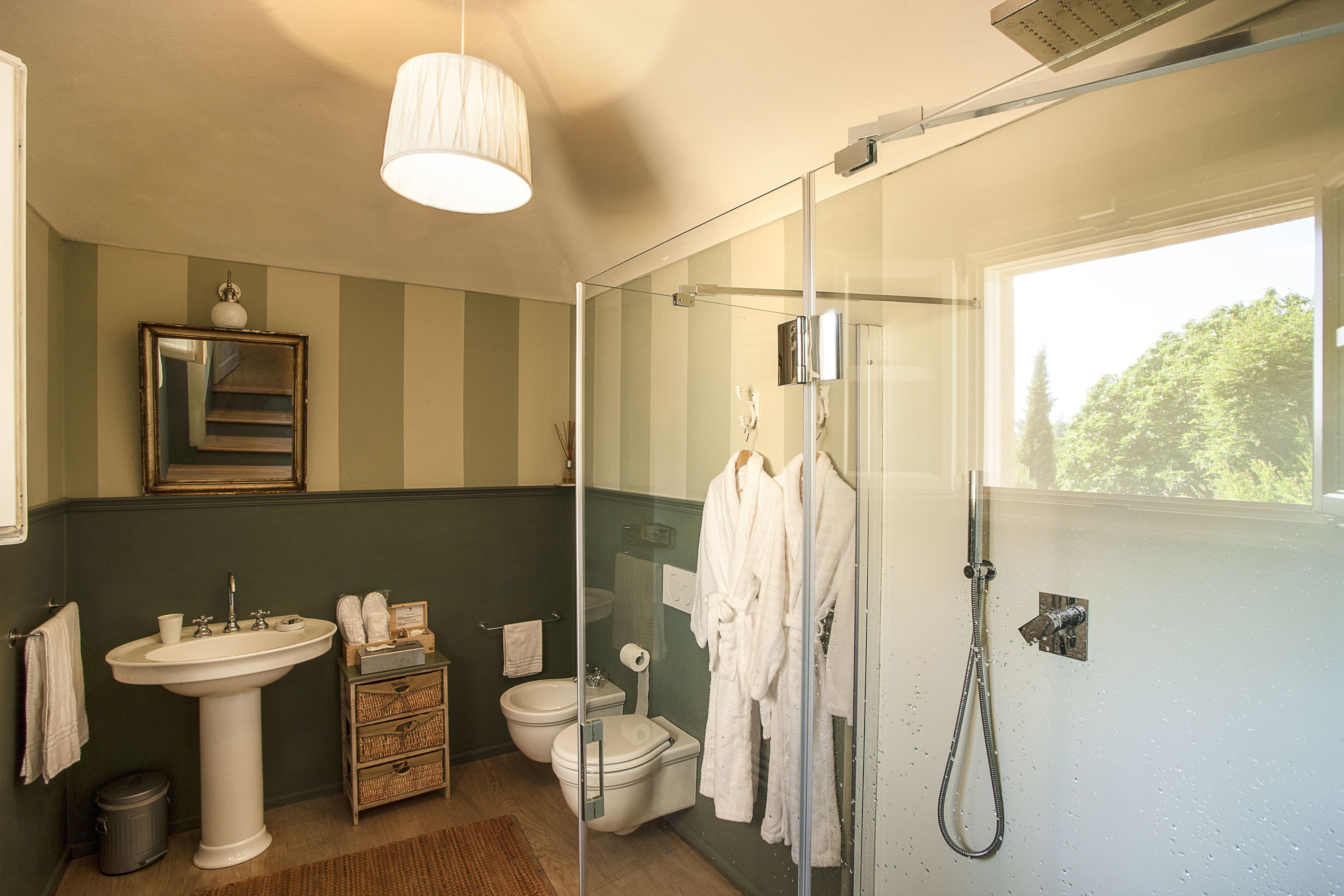 Baño con lavamanos pedestal, inodoro y cabina de ducha con mampara de vidrio.