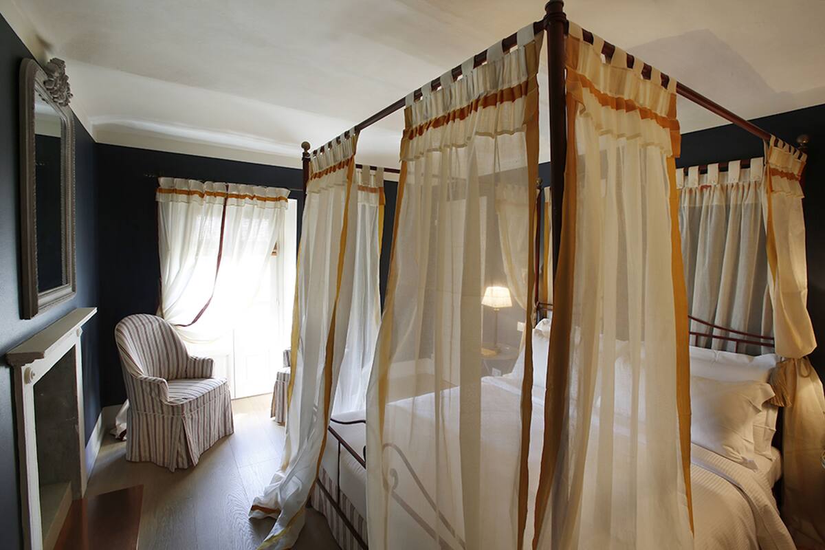 Een slaapkamer met een hemelbed, een stoel en een nachtkastje.
