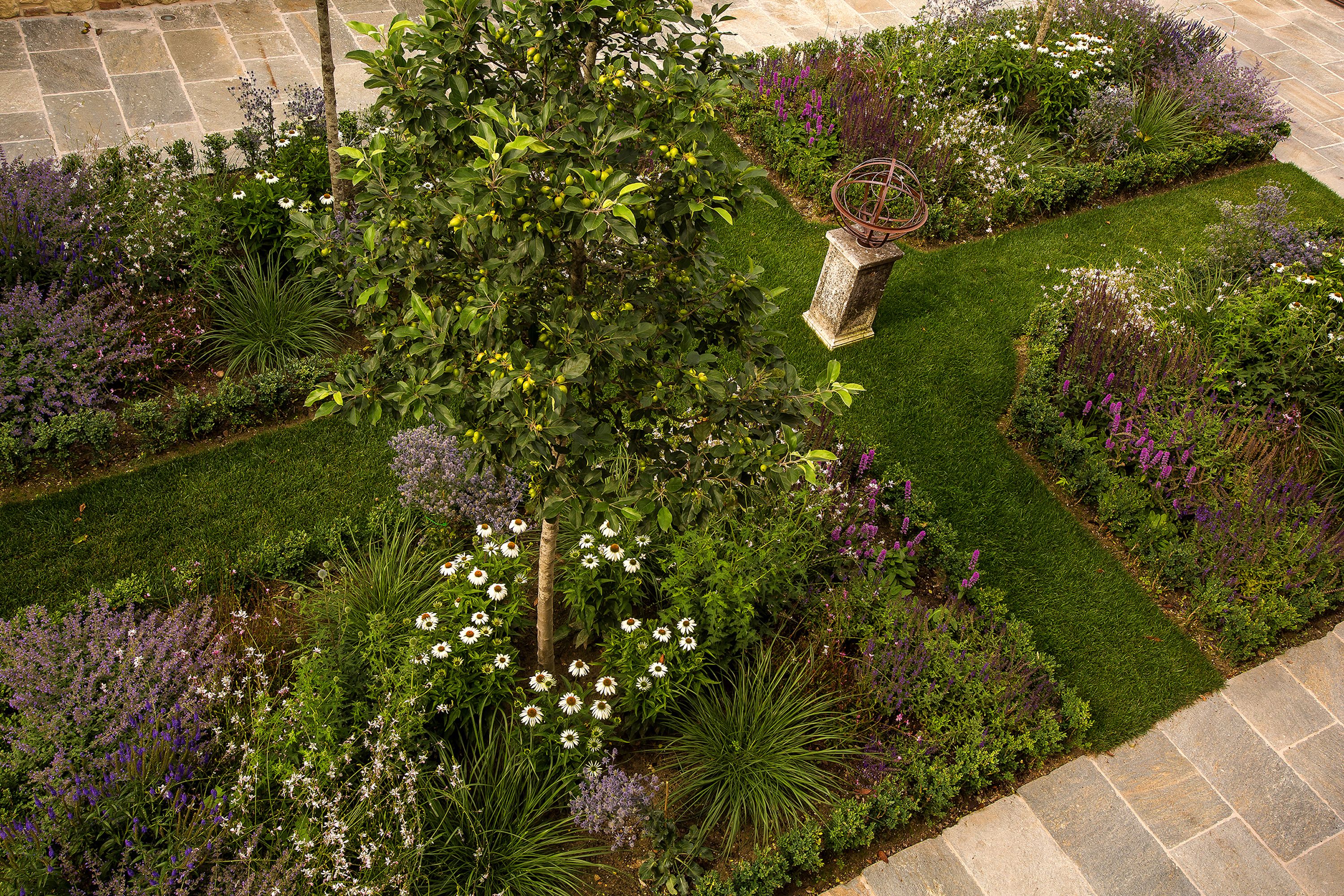 A well-maintained garden with a variety of plants and flowers, a stone pathway, and a decorative metal sculpture.