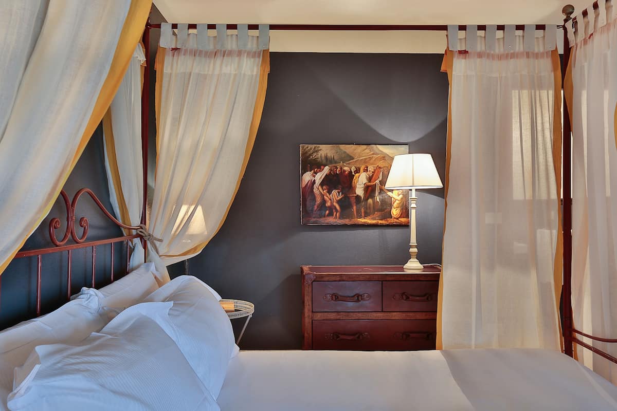 Een bed met baldakijn, een nachtkastje met lamp en een schilderij aan de muur.