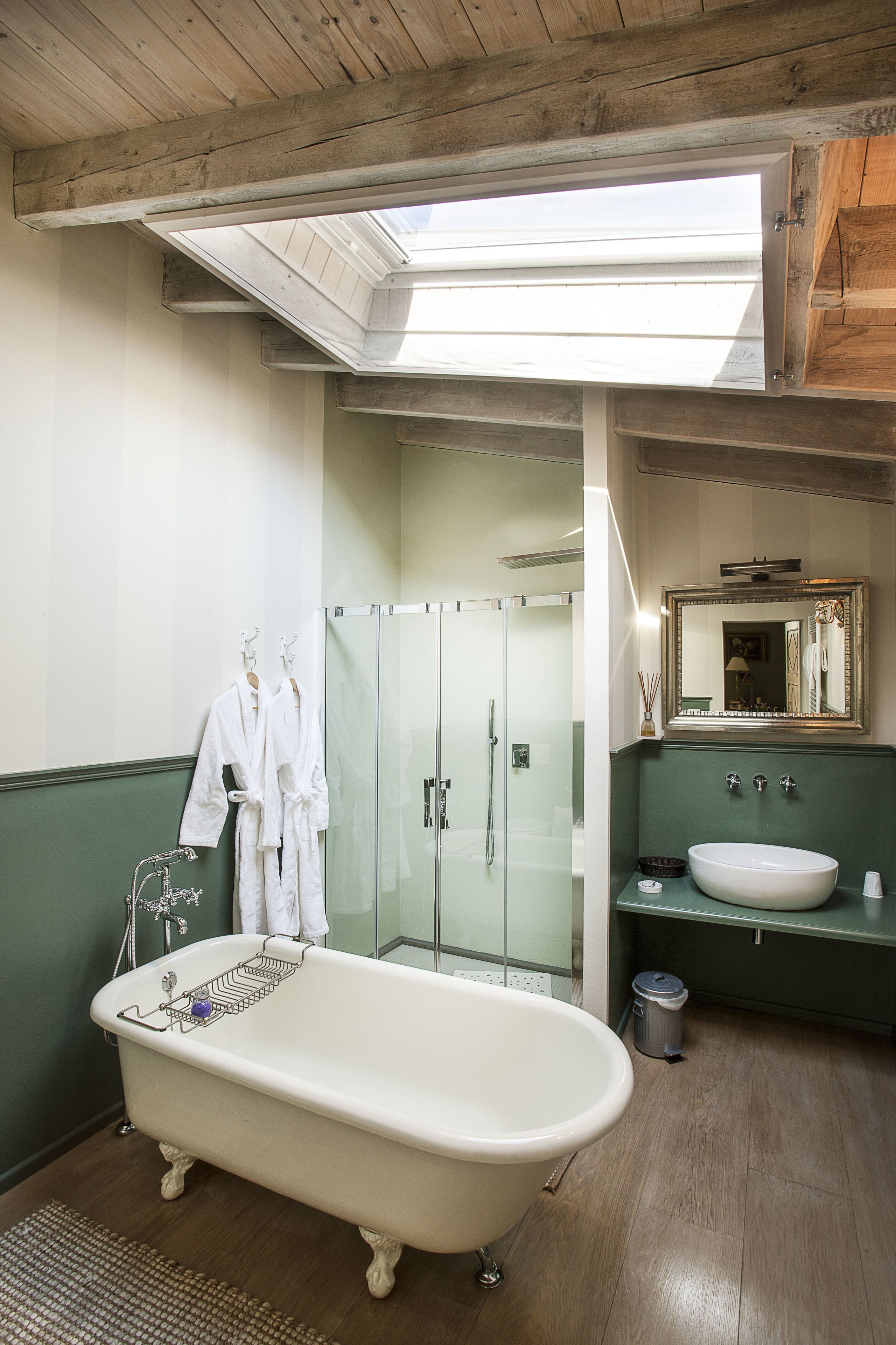 Ein Badezimmer mit freistehender Badewanne, einer Duschkabine, einem Waschtisch mit Spiegel und einem Oberlicht über der Dusche.