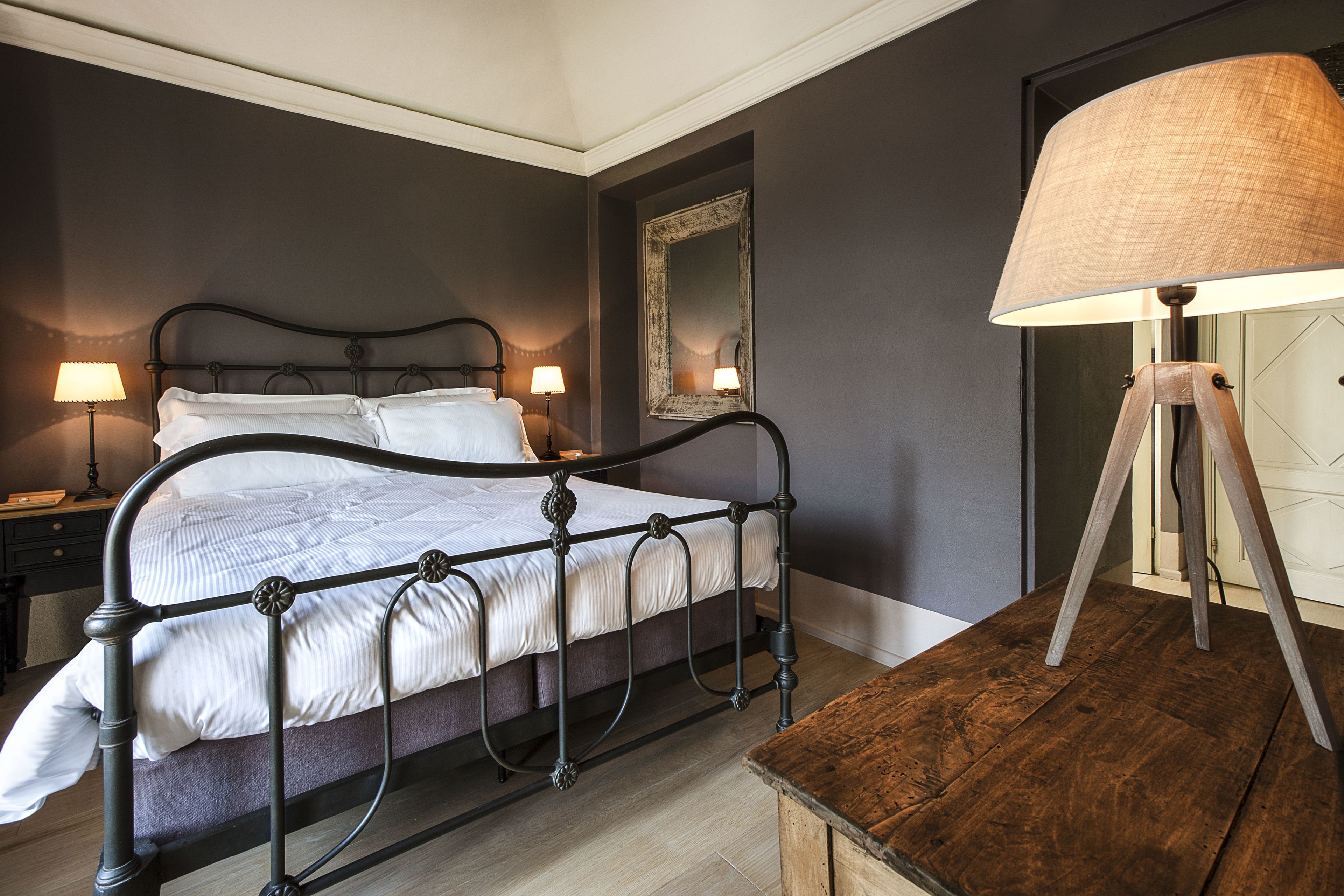 A neatly made bed with a metal frame, two bedside lamps, a wooden nightstand, and a large floor lamp.