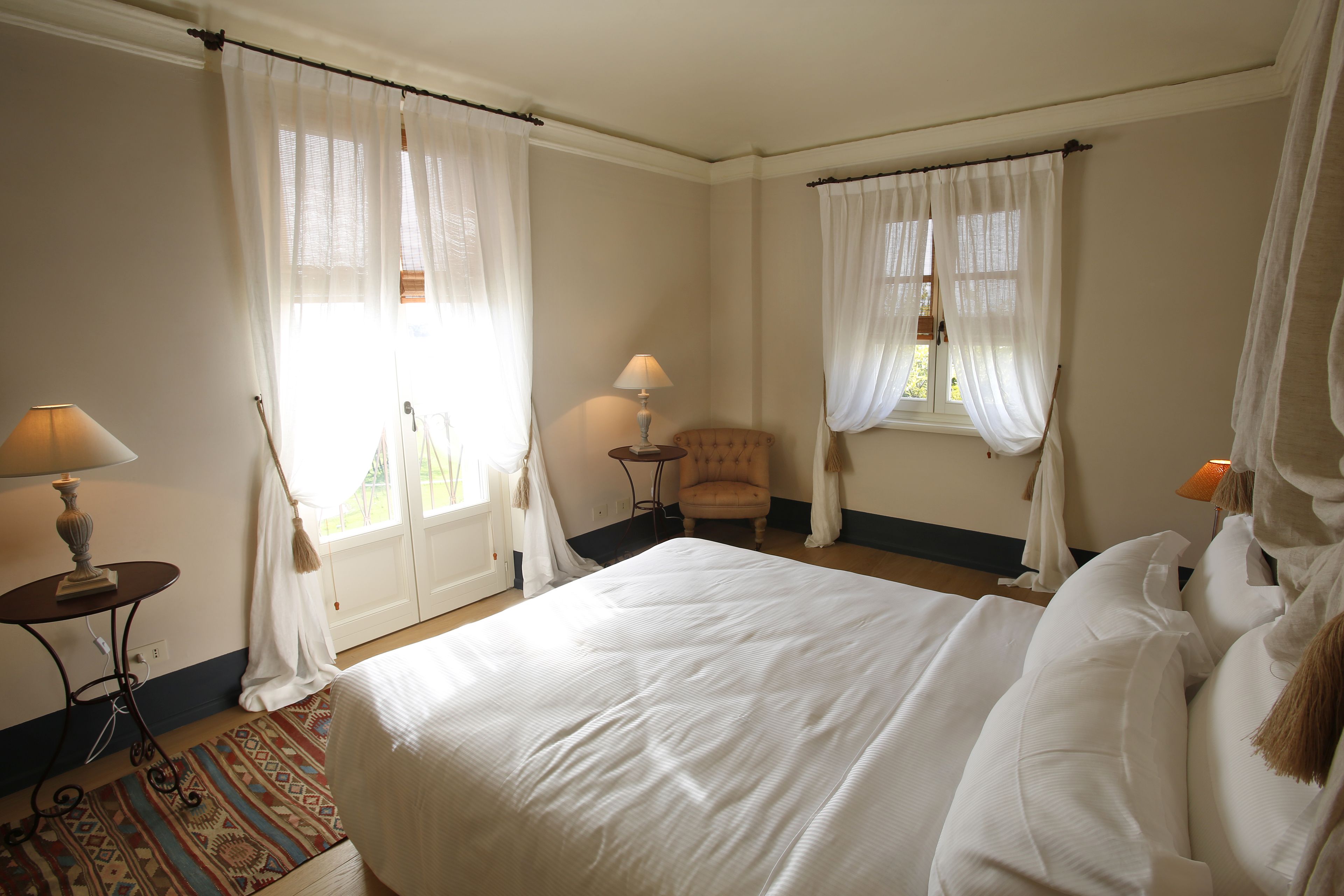 A hotel room with a large bed, two bedside tables with lamps, a chair, and a window with curtains.