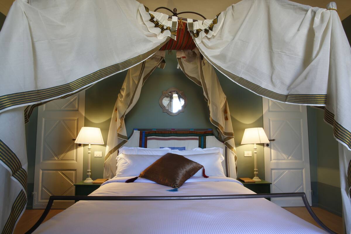 Een bed met hemel, twee bedlampen, een nachtkastje en een wandklok.