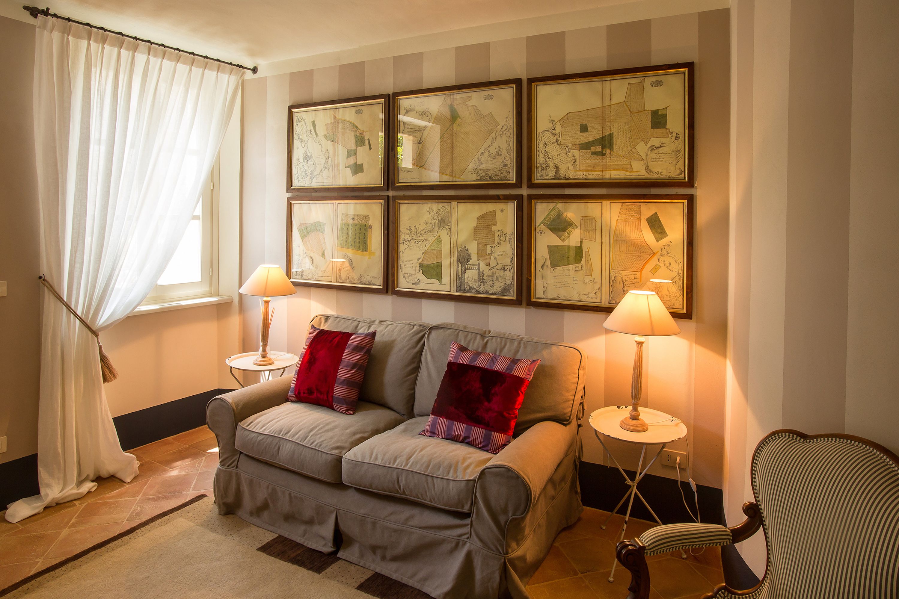 Una sala de estar con un sofá, dos mesitas de noche con lámparas, un sillón y un amplio ventanal con cortinas.
