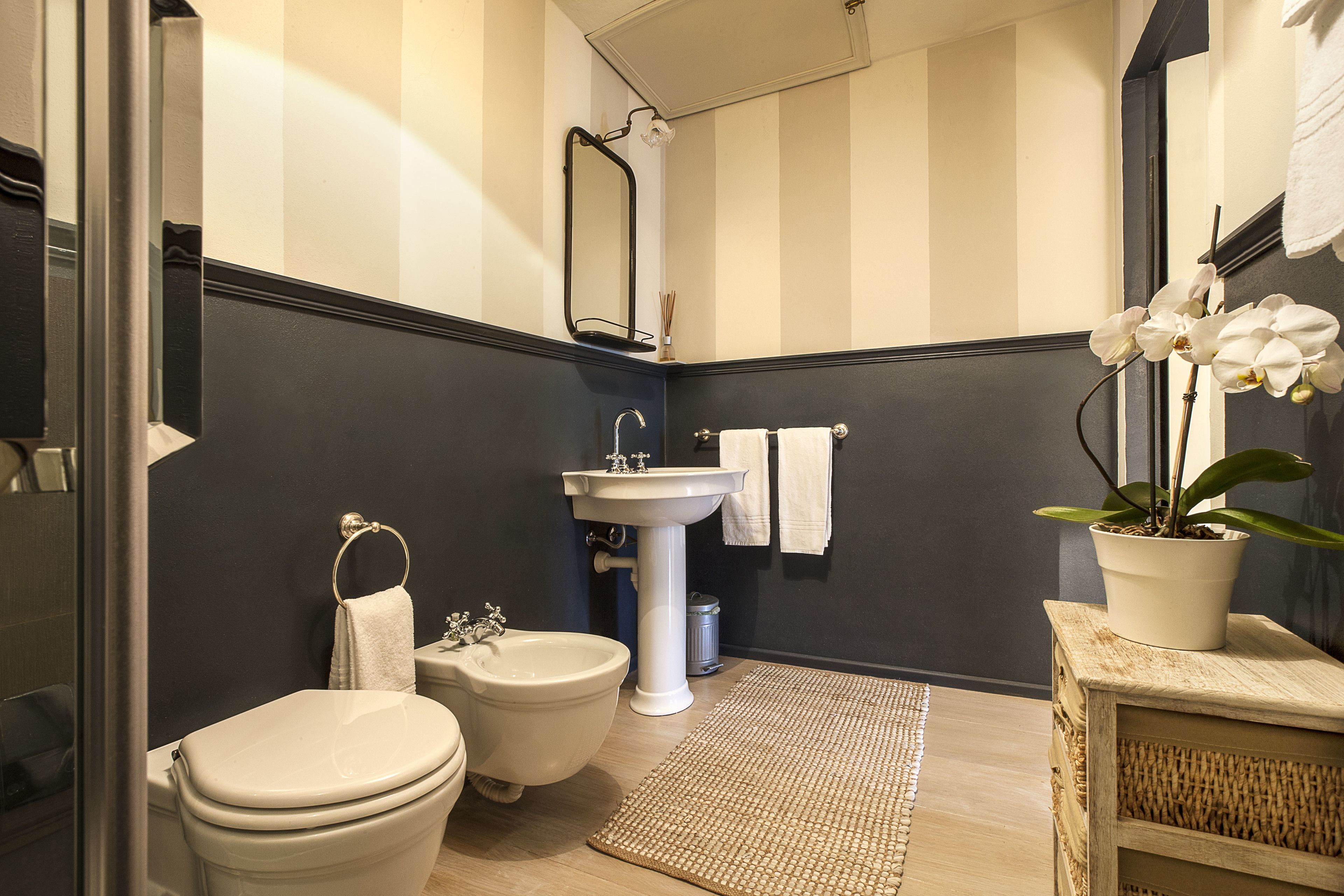 A bathroom with a toilet, bidet, sink, and a potted orchid.