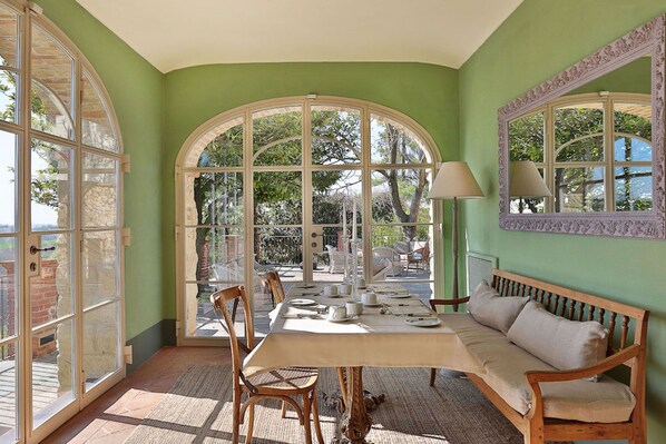 A dining area with a table set for four, surrounded by chairs, a bench, and a large arched window offering a view of the outdoors. - Relais Di Tenuta Santa Caterina (Grazzano Badoglio)