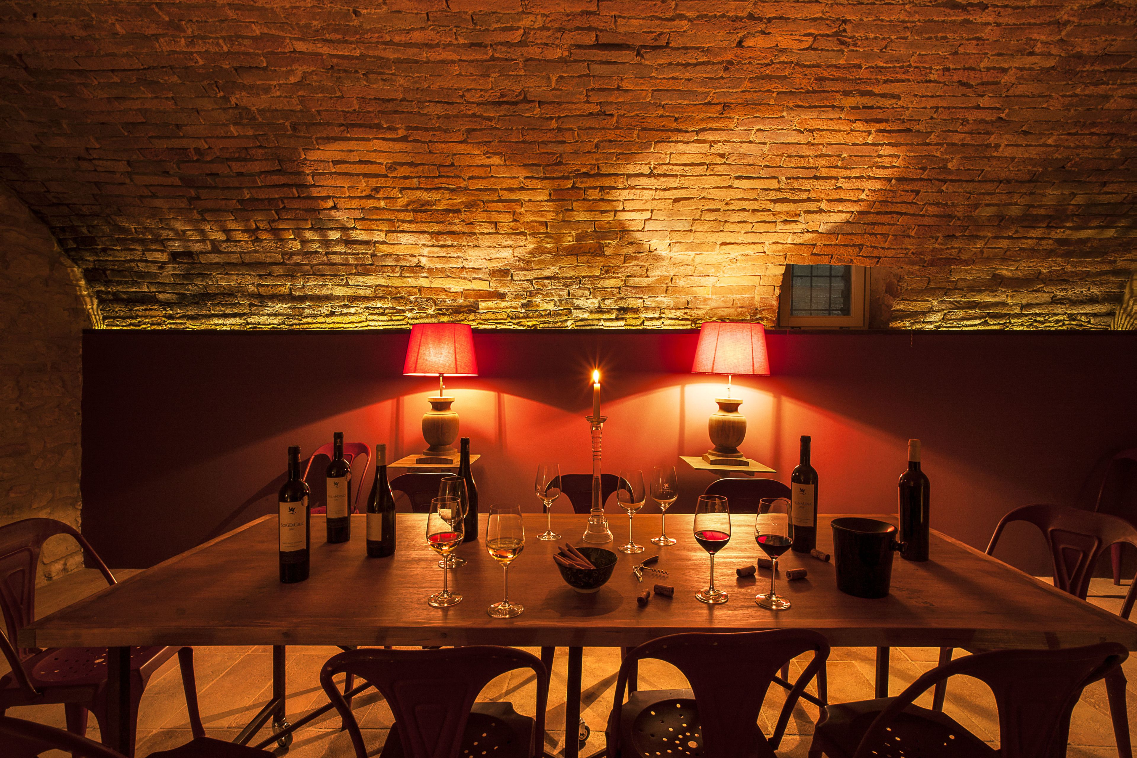 A dining area with a brick ceiling, a wooden table set for a meal, and two red lamps.