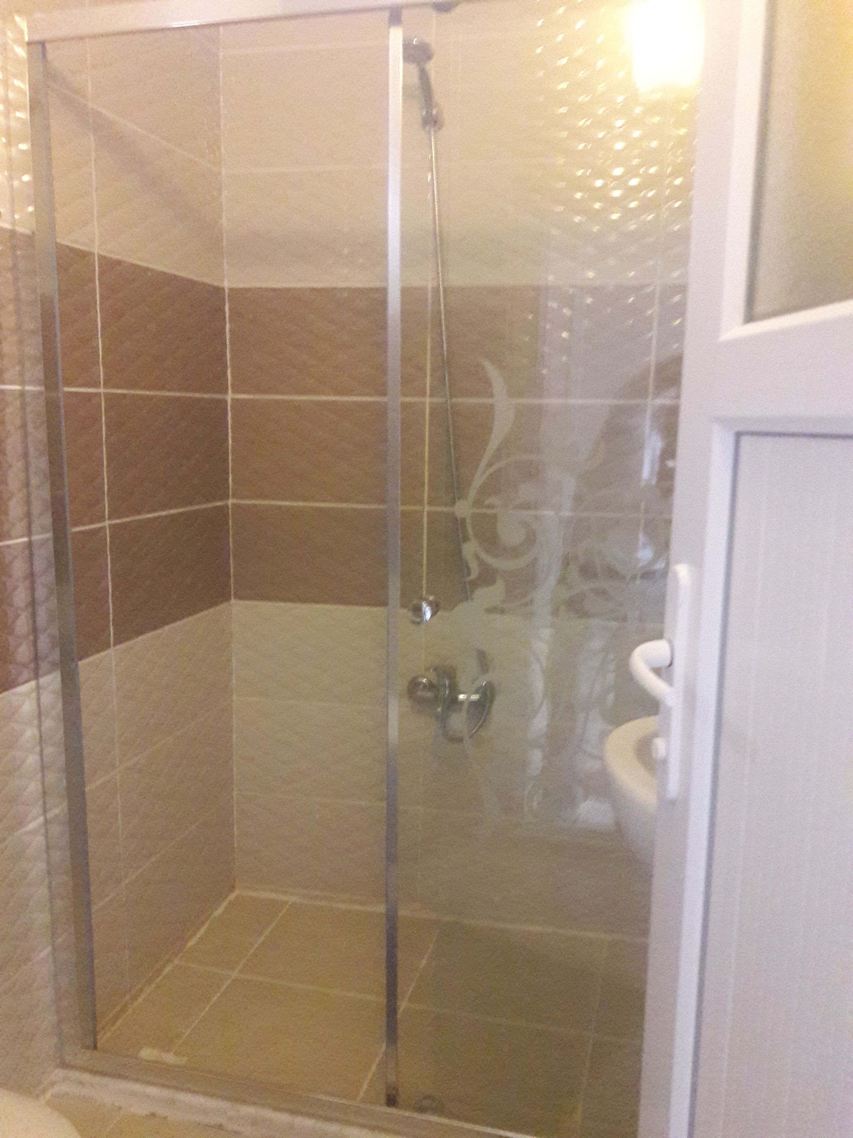 Ducha con mampara de vidrio, cabezal de ducha de mano y grifo empotrado.