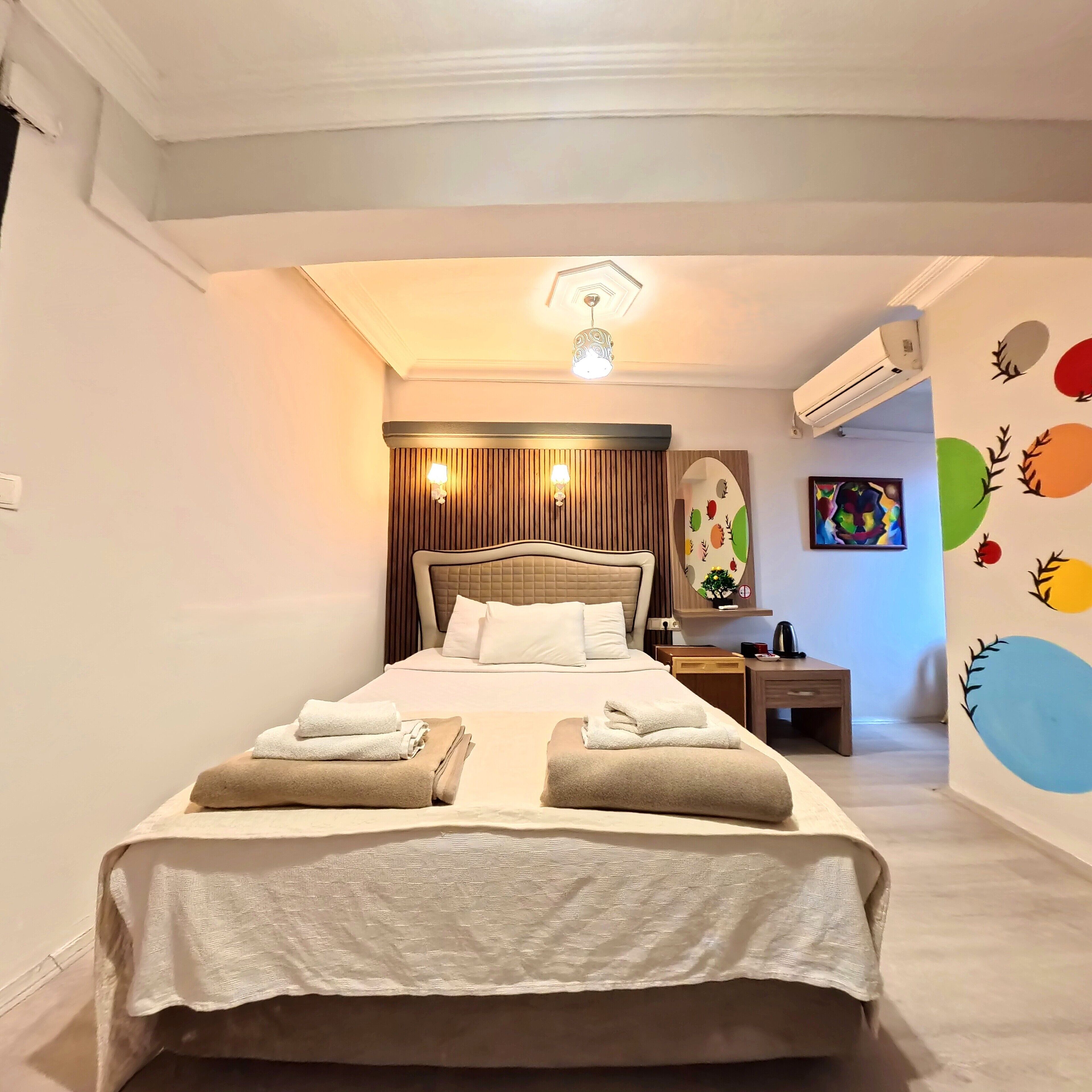 A neatly made bed with towels, a bedside table with a lamp, and a wall with colorful decals.