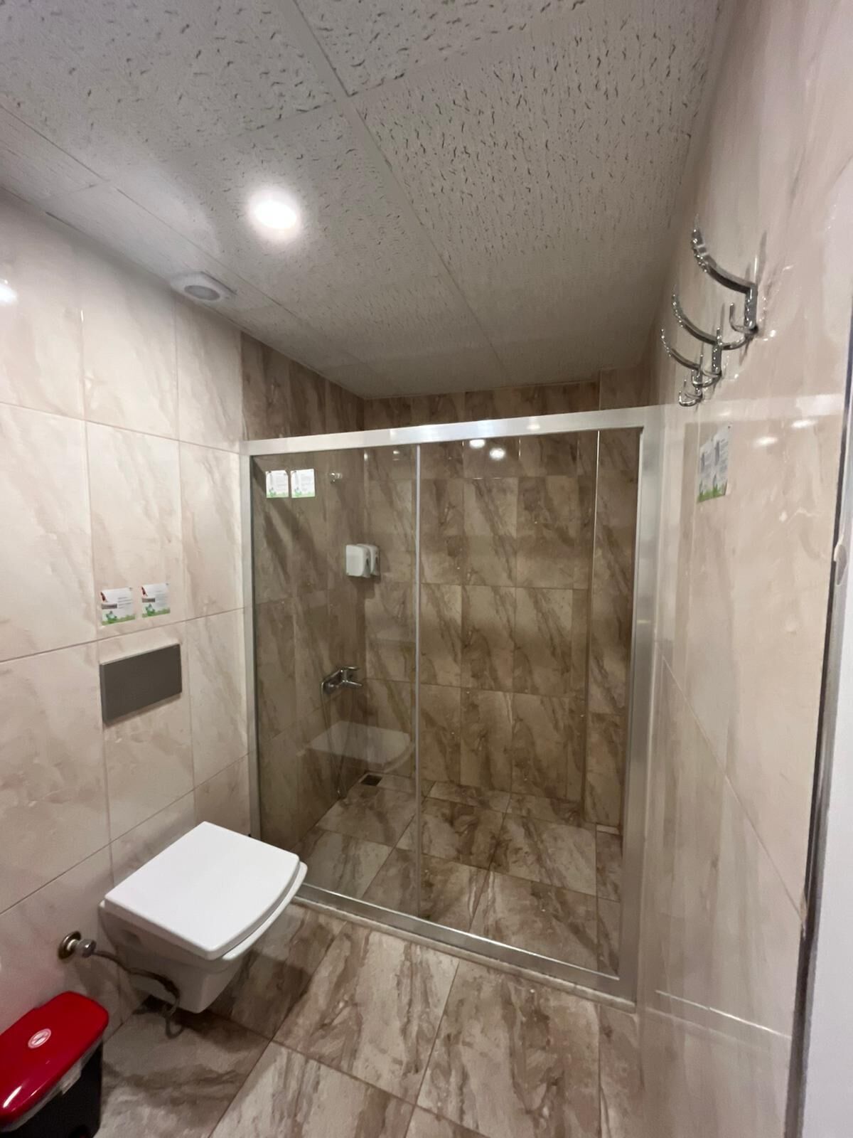 Un baño con ducha de vidrio, inodoro blanco y un cubo de basura rojo.