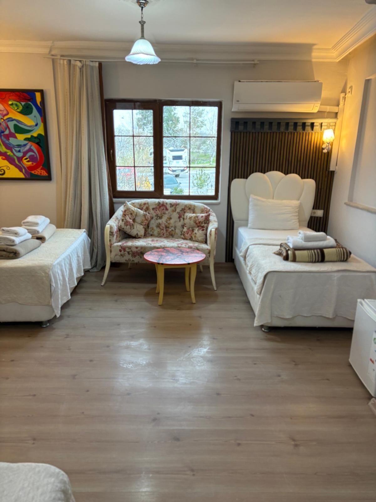 A hotel room with two beds, a floral sofa, a small round table, and a window with a view of the outside.