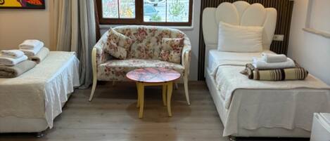 A hotel room with two beds, a floral sofa, a small round table, and a window with a view of the outside.