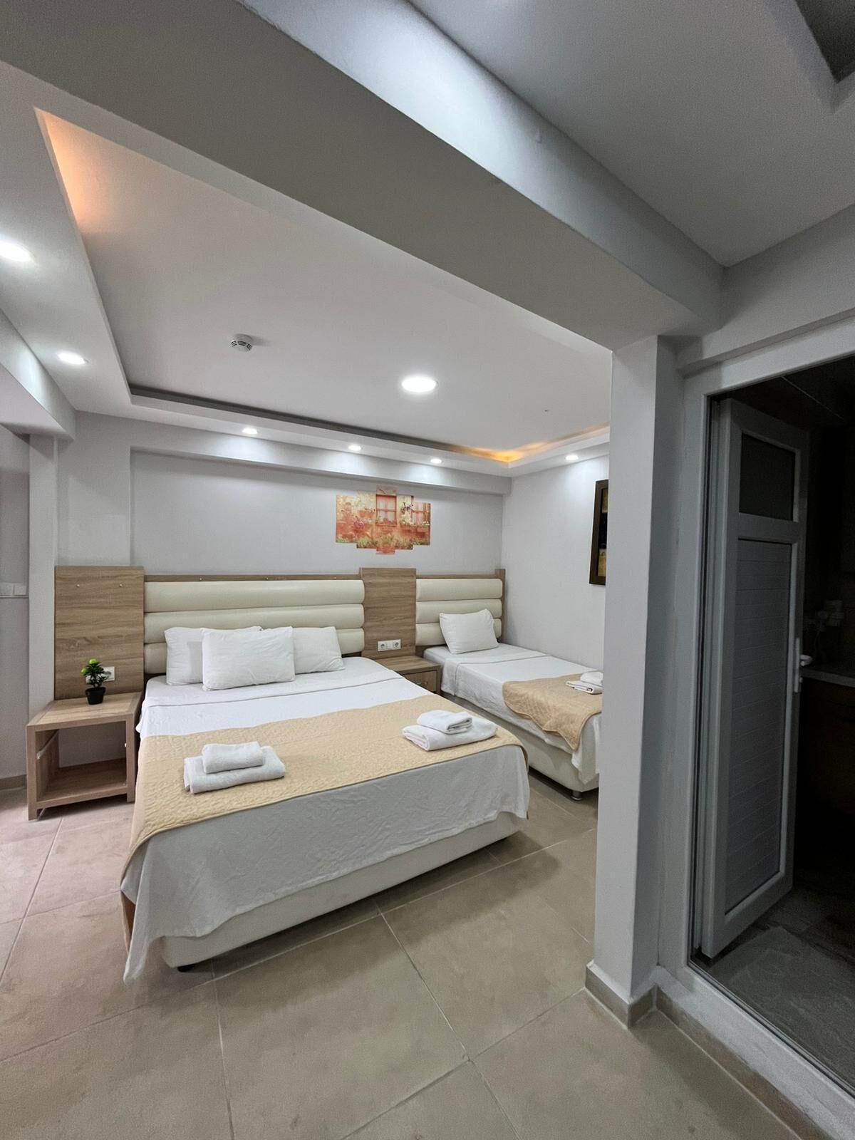 Une chambre d’hôtel avec deux lits, une petite table de chevet agrémentée d’une plante, une œuvre d’art accrochée au mur et une porte coulissante donnant sur un balcon.