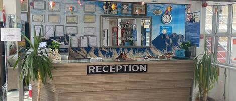 A reception desk with a 'RECEPTION' sign, framed certificates, and a mountain mural.