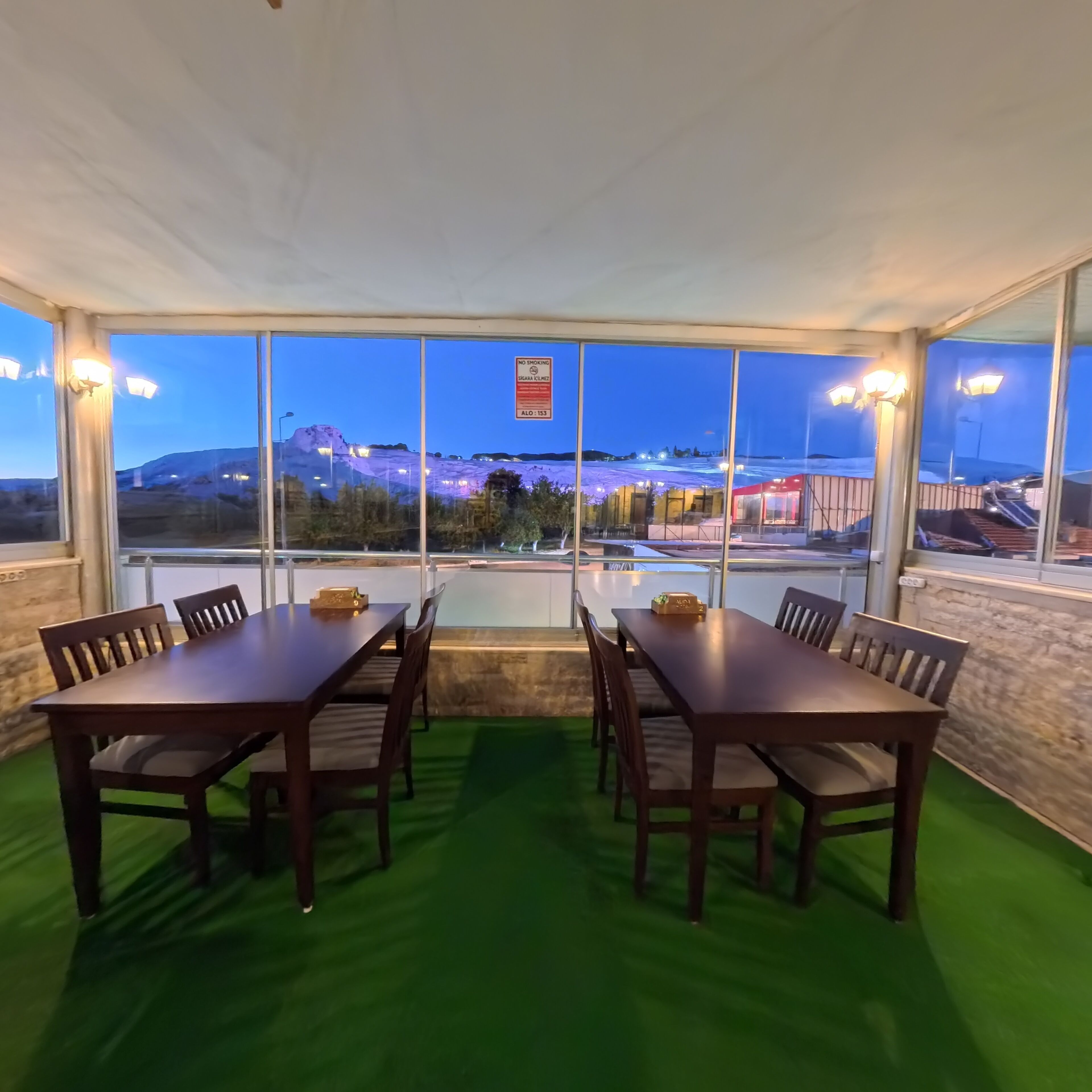 A conference room with a large table and chairs, large windows with a view of a mountain and a building, and a no smoking sign.