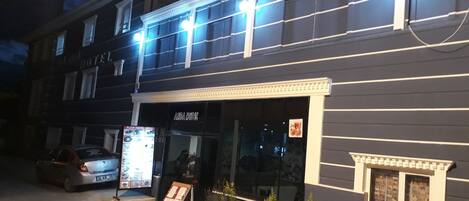 A two-story hotel with a dark facade, illuminated windows, and a visible restaurant sign outside.