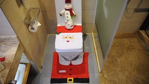 Een badkamer met een toilet versierd met een kerstmanfiguur, een rood-witte outfit en een sneeuwpop.