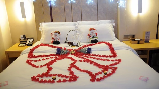 Een hotelkamer met een bed versierd met rode rozenblaadjes in de vorm van een hart, twee kerstmanbeeldjes en lichtjes in de vorm van sterren aan de muur.