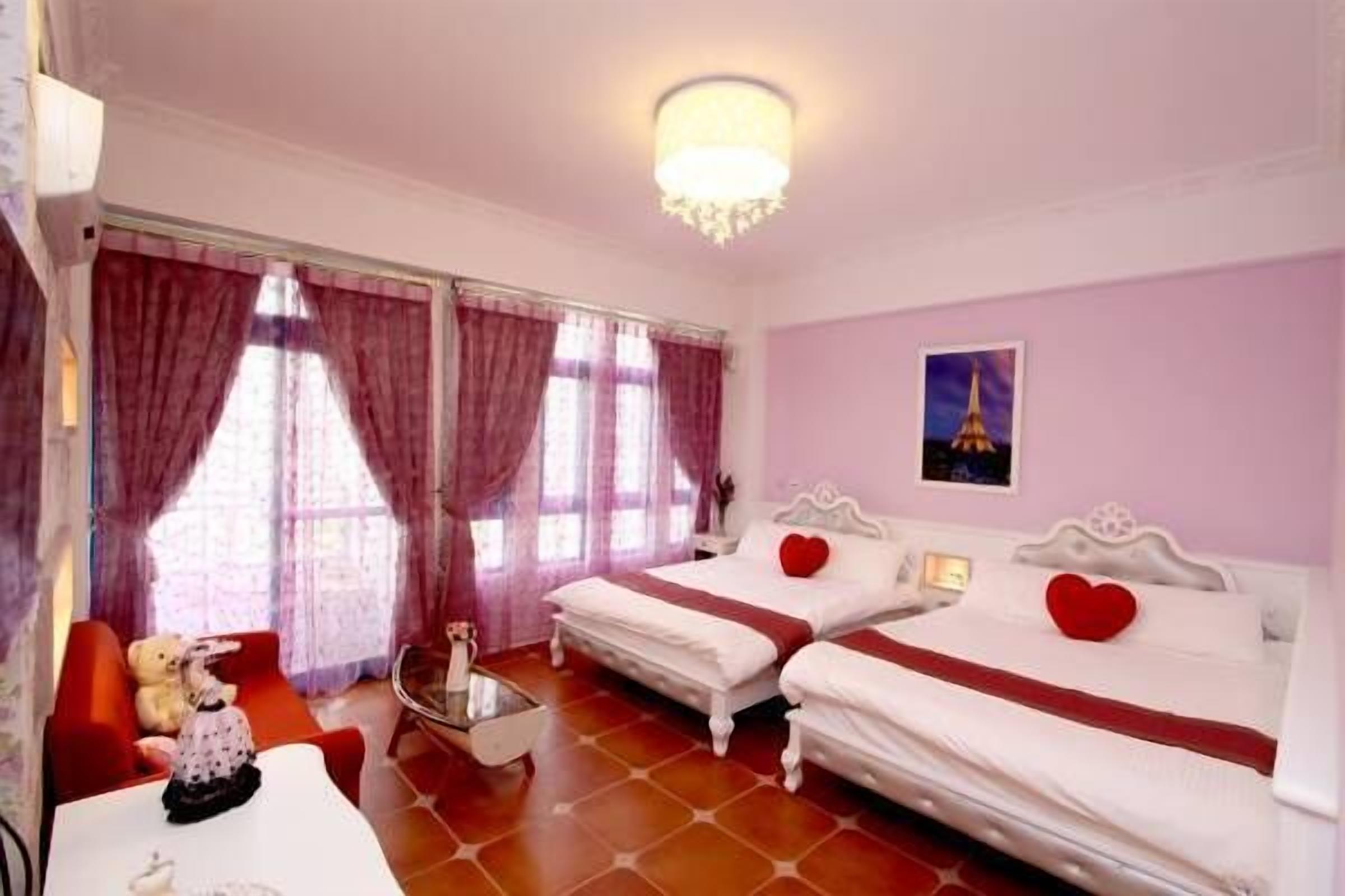Una habitación de hotel con dos camas, un sofá rojo, una mesita y un candelabro.