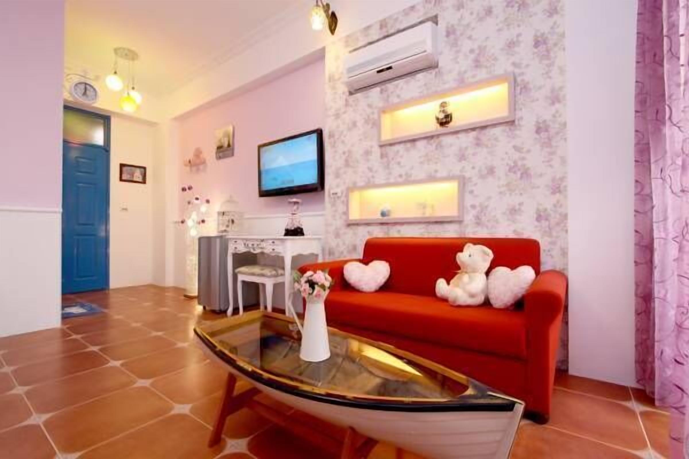 A living room with a red sofa, a glass coffee table, a television, and a floral wallpaper.