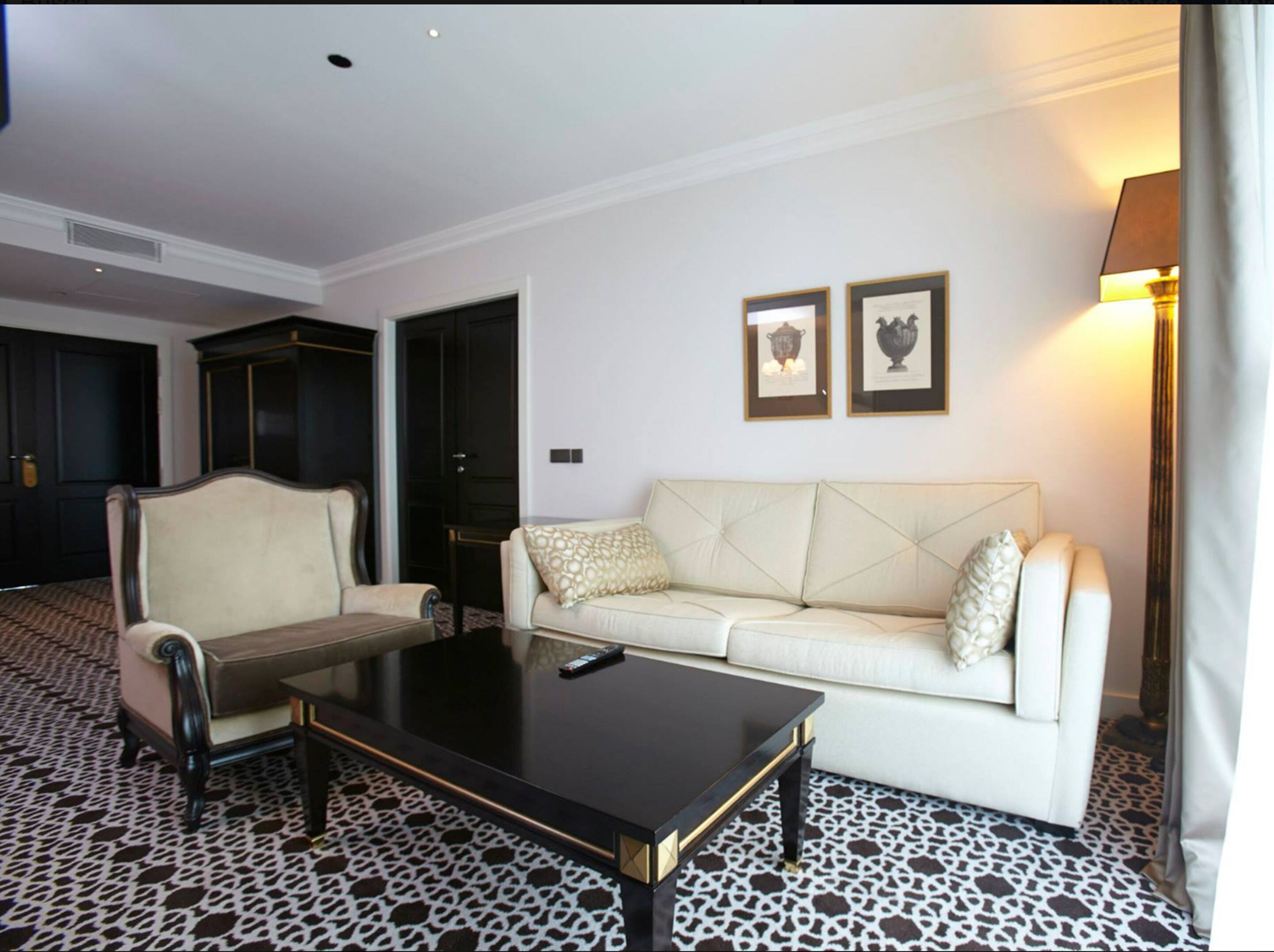 Een hotelkamer met een klassiek design, met een witte bank, een bijpassende fauteuil, een zwarte salontafel en een vloer met een patroon.