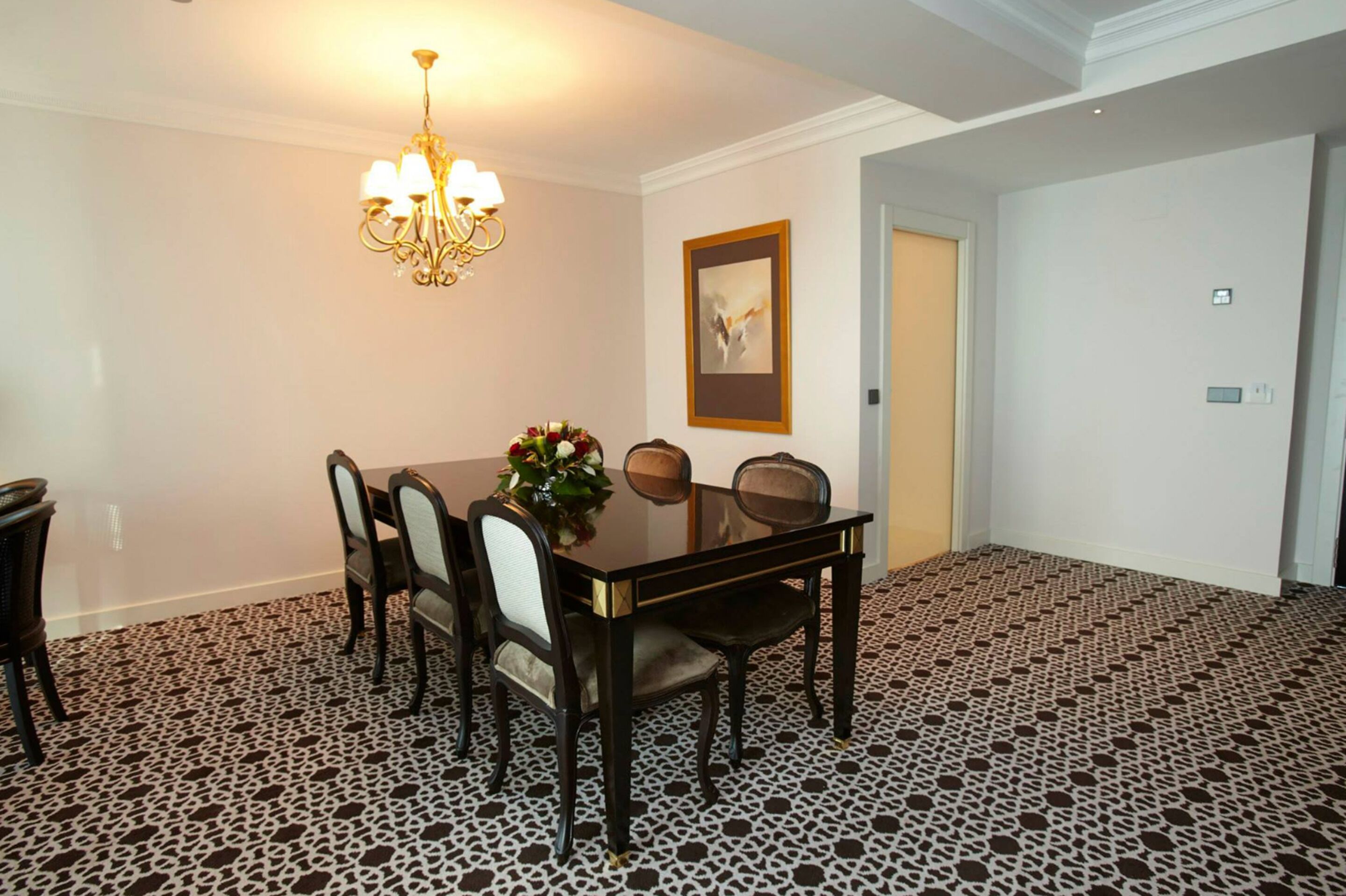 Een eetruimte met een tafel voor zes personen, een kroonluchter en een lijst aan de muur.