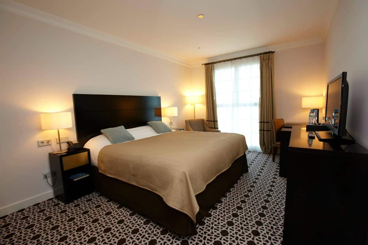 Habitación de hotel con una cama grande, dos mesitas de noche con lámparas, un escritorio con espejo y un televisor.