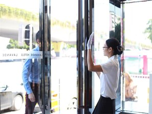 L’entrée d’un hôtel avec une porte en verre, une personne qui nettoie la vitre et un véhicule à l’extérieur.