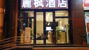 Entrada de un hotel con un letrero en caracteres chinos, una recepción y algunas personas adentro.