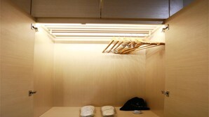 Un vestidor pequeño y bien iluminado con un banco de madera, un perchero y ropa doblada cuidadosamente.