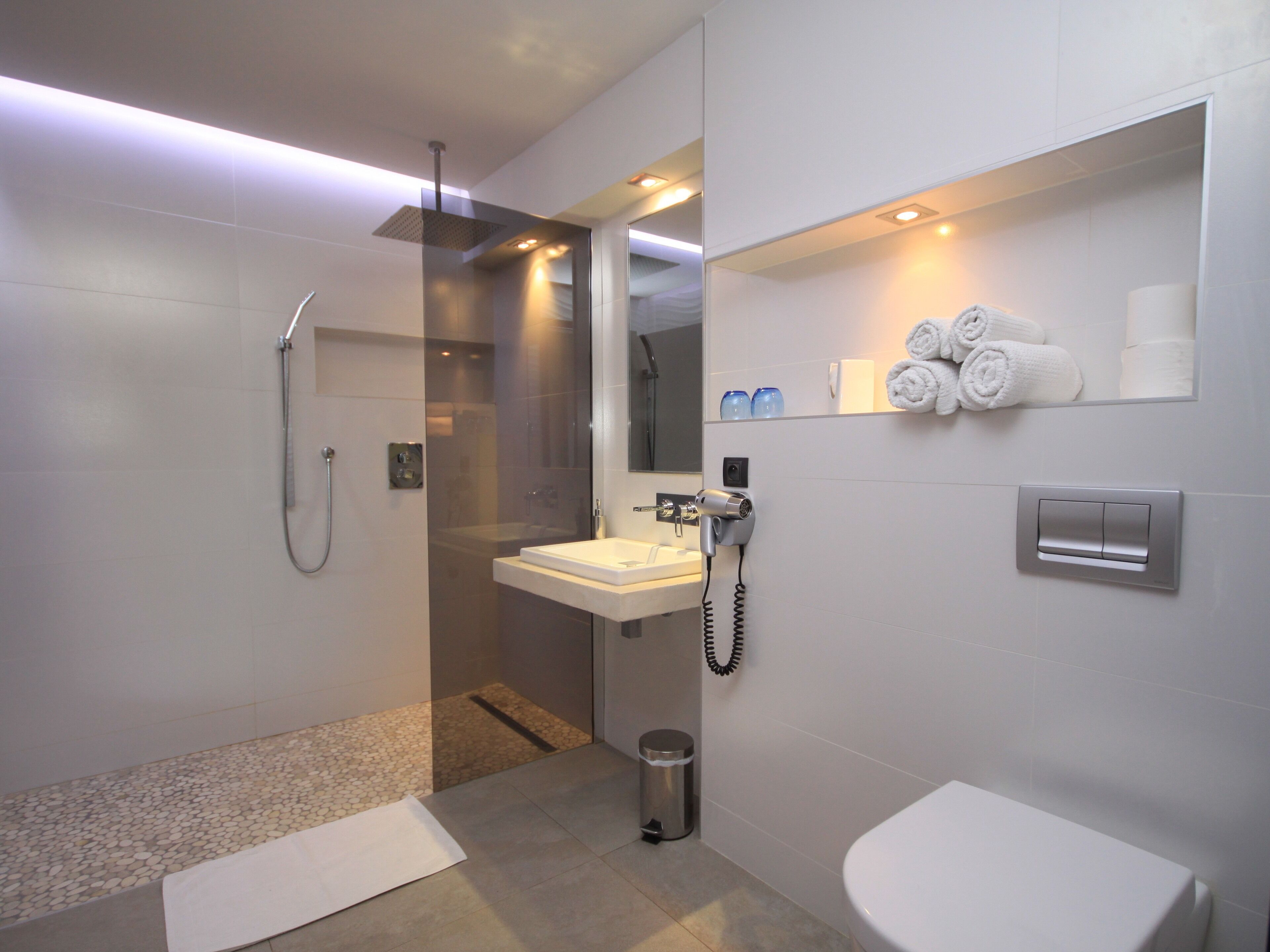 Een moderne badkamer met een douchecabine van glas, een wastafel, toilet en een handdoekrek met handdoeken.