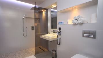 Een moderne badkamer met een douchecabine van glas, een wastafel, toilet en een handdoekrek met handdoeken.