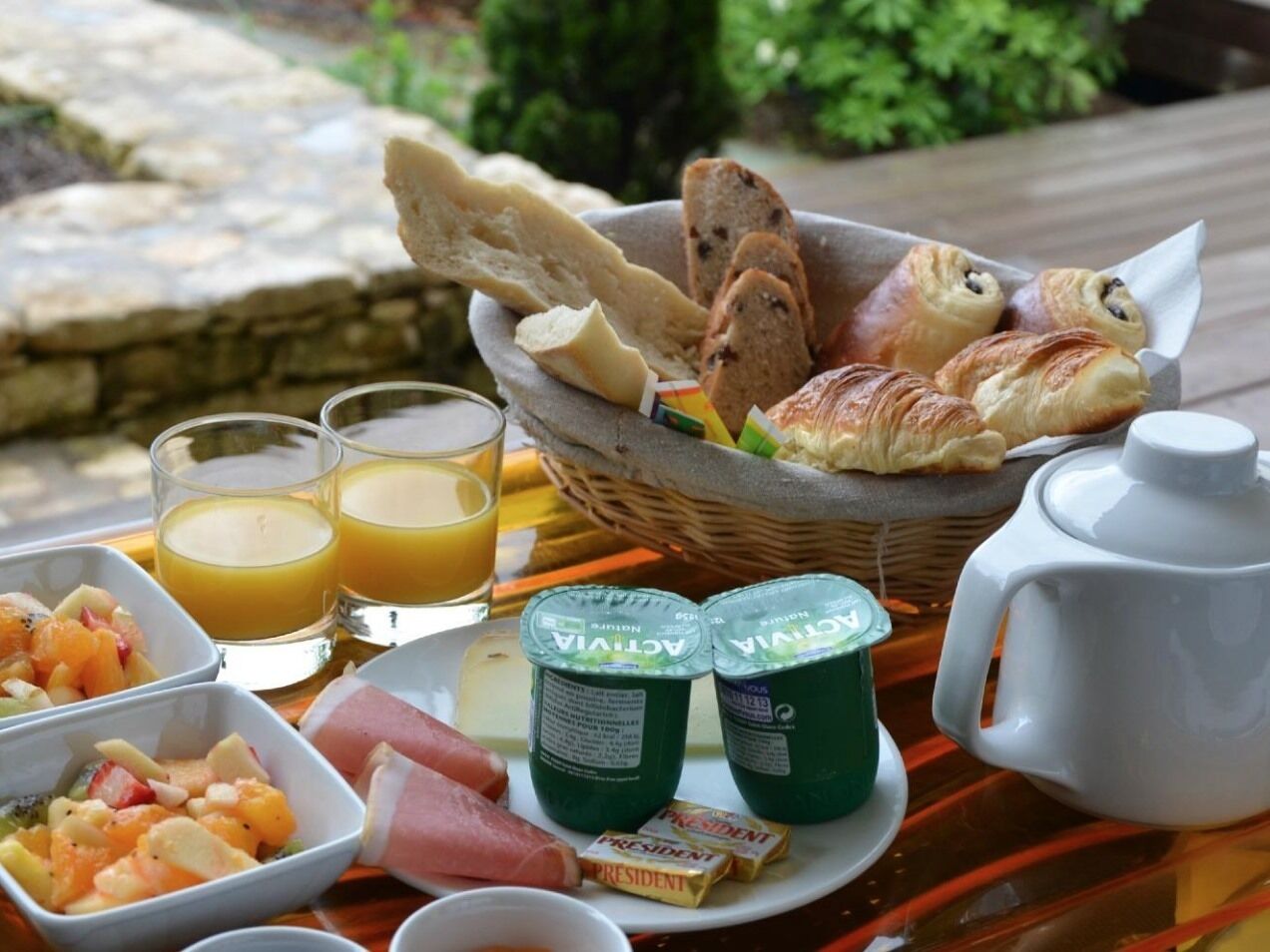 A breakfast tray with croissants, bread, yogurt, ham, fruit, and juice.