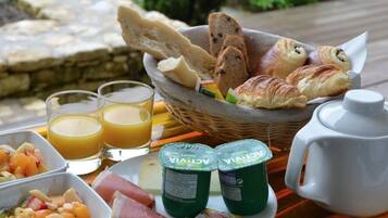 A breakfast tray with croissants, bread, yogurt, ham, fruit, and juice.